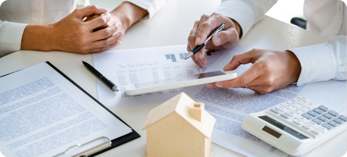 Close up of a desk with papers on it, and two people's hands flipping through a comparative market analysis to compare it to an online home value estimate.