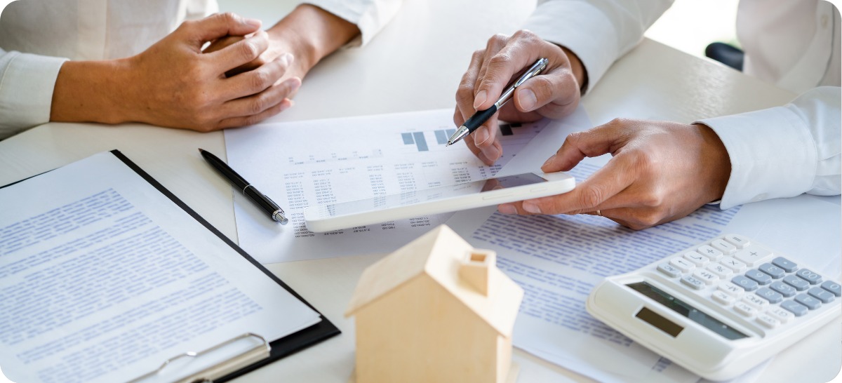 Close up of a desk with papers on it, and two people's hands flipping through a comparative market analysis to compare it to an online home value estimate.