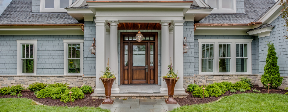 Exterior of a house with pale blue shingle siding and a wooden entry door with a transom window.