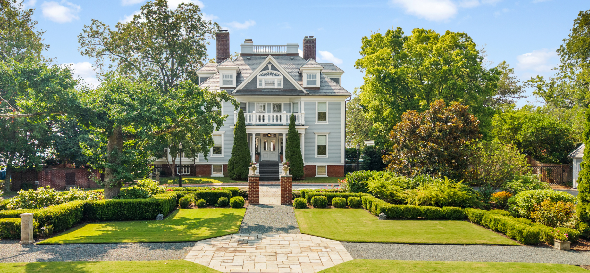 1900's light gray Victorian style home with white trim, two balconies, and a widow's walk flanked by two brick chimneys.